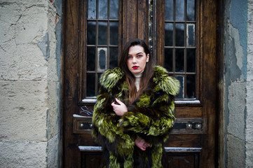 Brunette girl in green fur coat against old wooden doors.
