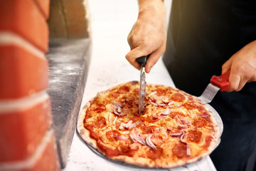 cook hands cutting pizza to pieces at pizzeria