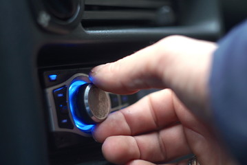 Man's hand tuning radio in the car. 