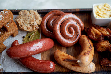 Meat set for a large company on a wooden stand. Grilled sausages, sauerkraut, French fries and sauces