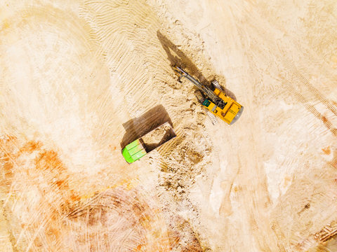Aerial view of excavator loading dump truck with raw kaolin in kaolin open pit mine for ceramic tiles production. Industrial area from above. Industrial mining background texture concept.