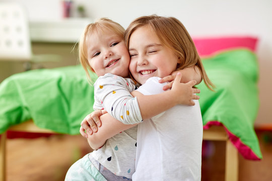 happy little girls or sisters hugging at home