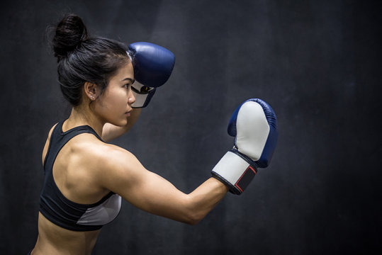 Beautiful young Asian woman posing with blue boxing gloves, black background