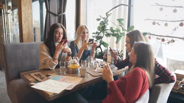 Four beautiful women sit in cafe with phones