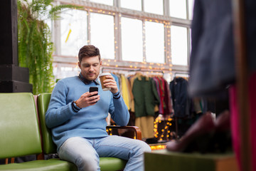 man with smartphone and coffee at clothing store