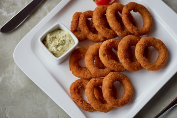 Golden onion rings fried in deep frying. With Sauce on a white plate