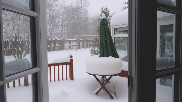 Deep snow in a garden viewed through open double glazed French doors.
