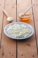 Cheese, fresh cottage cheese in a white plate, wooden spoon, cottage cheese and honey on a wooden background, sour cream in a wooden spoon, dairy products on a natural background, retro style