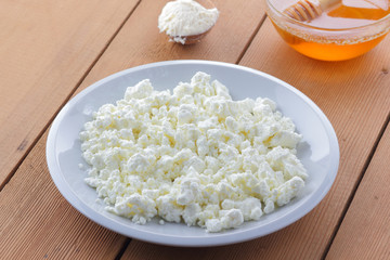Cheese, fresh cottage cheese in a white plate, wooden spoon, cottage cheese and honey on a wooden background, sour cream in a wooden spoon, dairy products on a natural background, retro style
