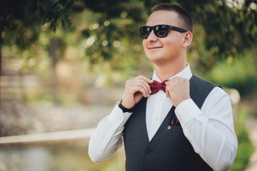 Closeup of adult handsome smiling groom in white shirt adjusting