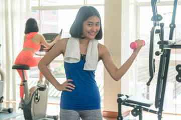 Fototapeta premium Beautiful woman wearing blue and gray sportswear while holding dumbbells. fitness slim young woman lifting weights in gym. concept of exercise.