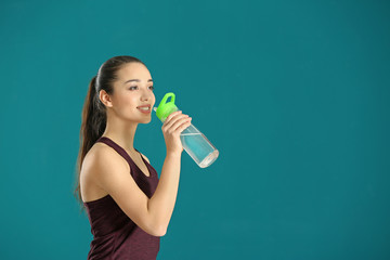 Beautiful young woman drinking water after doing fitness exercises on color background