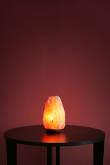Himalayan salt lamp on table against color background