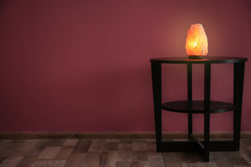 Himalayan salt lamp on table near color wall
