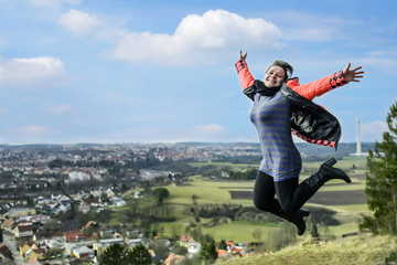 young sweet girl in open clothes with arms outstretched smiling in flight on a high hill.