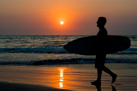 surfer walking on beach at sunset