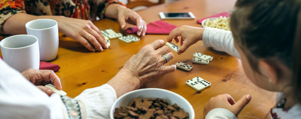 Unrecognizable grandmother, daughter and granddaughter playing domino in the living room