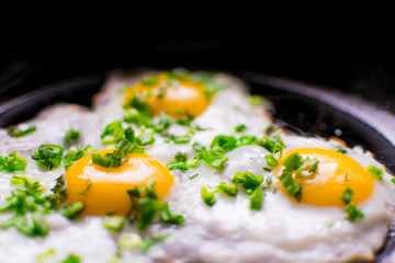 Fried chicken eggs with greens and spring onions in a frying pan.