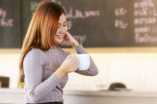 Smiling woman with a cup of coffee in her hands sits in a modern cafe.