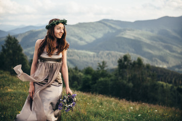 A beautiful girl in a dress and a bouquet of flowers in her hands, on a green glade dancing among the peaks of the mountains
