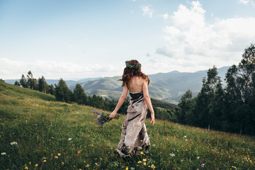 A beautiful girl in a dress and a bouquet of flowers in her hands, on a green glade dancing among the peaks of the mountains