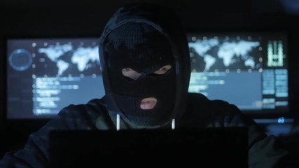 Dangerous hacker in the mask tries to enter the system using codes and numbers to find out the security password. The concept of cybercrime.