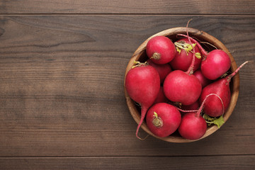 fresh red radishes in wooden bowl on the brown table with copy space