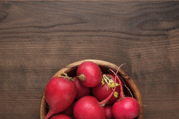 fresh red radishes in wooden bowl on the brown table with copy space