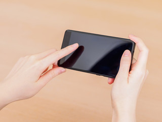 Girl pointing finger on screen smartphone on wooden table background in office.