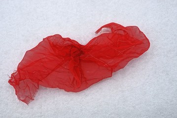 кусок красной мятой  яркой ткани на белом снегу