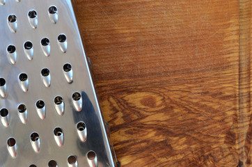 The chrome grater lies on the cutting board with a lot of scars from the ax and knife. Background...