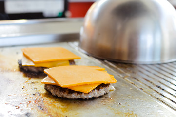 Closeup on cheeseburger preparing with cheese melts on the stove background