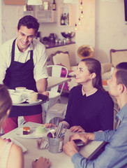 smiling waiter bringing ordered dishes to friends in tearoom