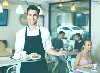 Waiter holding served tray meeting visitors at pastry bar