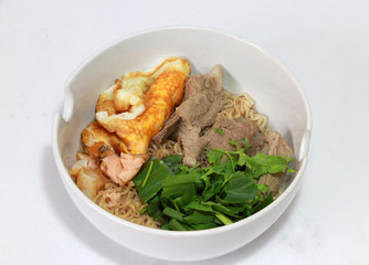 Boiled instant noodles with pork rip, fried egg, fish meat and green vegetable in the white bowl. Simple cooking at home.