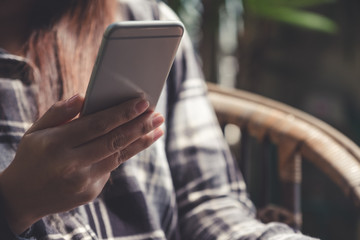 Closeup image of a beautiful Asian woman holding , using and looking at smart phone while sitting in outdoor