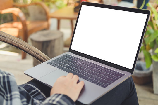 Mockup image of hands using and typing on laptop with blank white desktop screen , sitting outdoor on wooden chair and green nature background