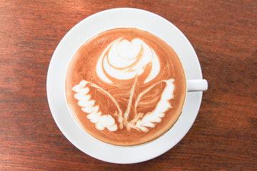 A cup of coffee with a beautiful rose on the wood arranged in the middle.