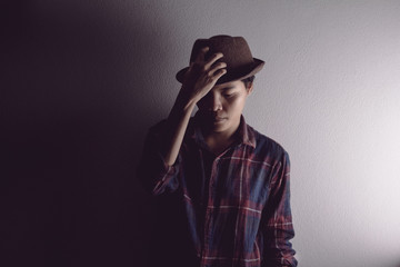 A man in a plaid shirt looks sad and holds a brown vintage hat.