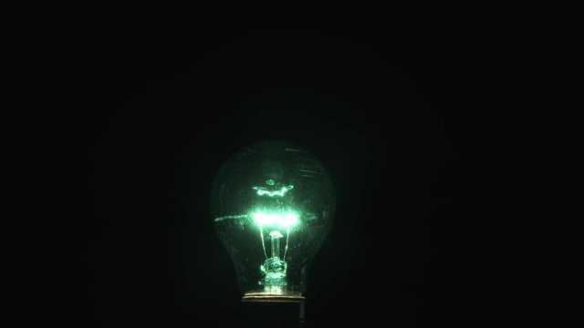 Close up on green colored party bulb against black background with light turning on and off with flicker, seamless looping.
