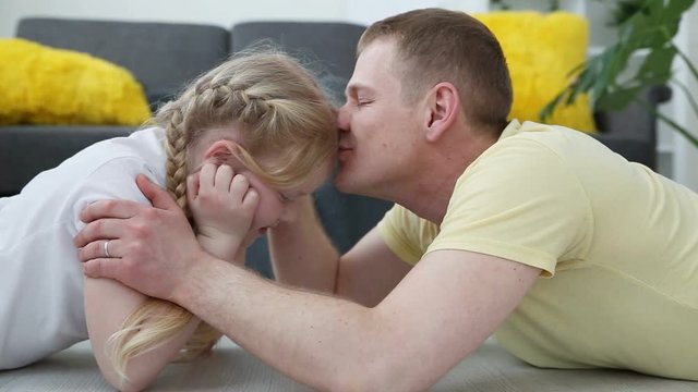 care for children in the family. Dad kisses and hugs a little daughter, lying on the floor in the living room.