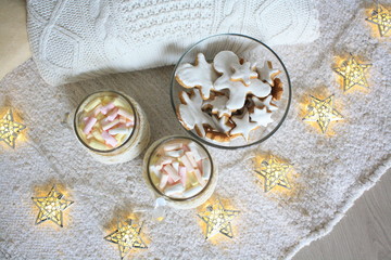 Gingerbread cookies & white knitted sweater festive garland decor background. Tasty sweet homemade cookies with white fudge or glaze, marshmallow in glass. Holiday warm knitting & ginger bread cookies