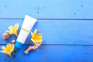 Zelfklevend Fotobehang Beach accessories. Blank sunblock/moisturizer, plumeria flowers, sea shell on blue wooden background © selinofoto