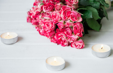Beautiful pink roses with candles on a white wooden surface