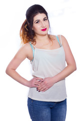 Obraz premium Studio portrait of a beautiful young woman with black hair gathered in a tail. A girl in a T-shirt and jeans poses against a white background. He looks at the camera. Isolate