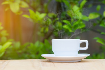 hot coffee with steam on wooden table and blurred green plant background. Copyspace