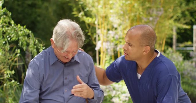 4K Care assistant offering support to crying senior man in nursing home garden