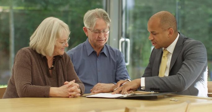 4K Senior couple signing a document in a meeting with financial adviser