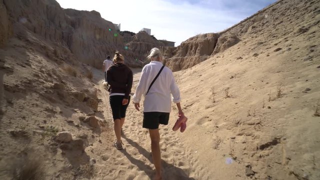 Grandmother, daughter, and grandson all walk up a sandy eroding canyon on a warm morning.