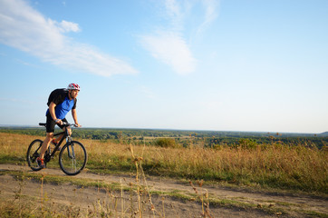 Obraz premium Male cyclist with backpack driving by rural dirt road outdoors